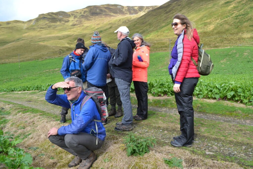 People in a group, standing together in the landscape, green and hilly.